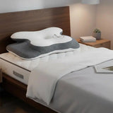 Oreiller cervical ergonomique blanc et gris sur lit, forme sculptée pour le cou.